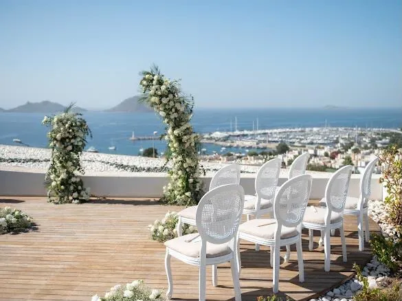 Terrace wedding ceremony with white chairs and floral arches overlooking Turgutreis marina